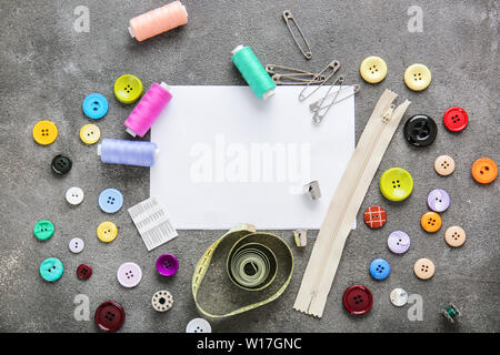 Set di fili di cucitura con accessori e di un foglio di carta su sfondo grigio Foto Stock