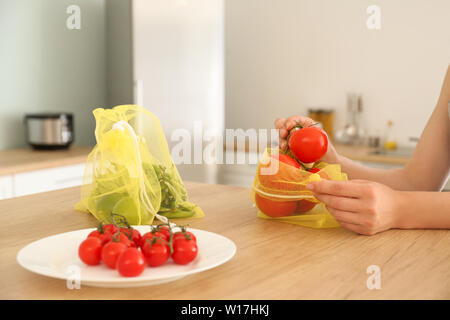 Donna di mettere i pomodori freschi in eco bag in cucina Foto Stock