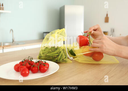 Donna di mettere i pomodori freschi in eco bag in cucina Foto Stock