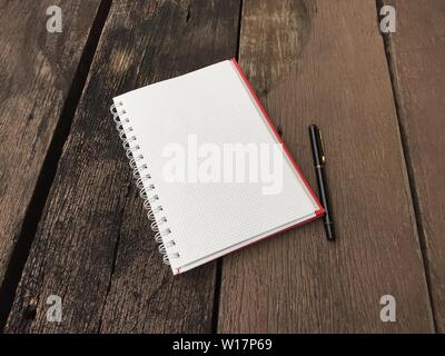 Pagina del notebook e penna nera sul vecchio tavolo in legno con sfondo spazio copia. Blank aprire Blocco note sul foglio di legno scuro superficie. Vista superiore della nota aperta boo Foto Stock