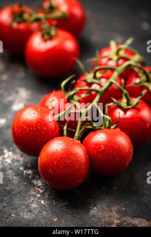 Pomodori ciliegia sulla vite scuro su sfondo arrugginito. Orientamento verticale Foto Stock