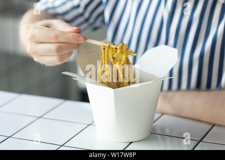 Close-up di un giovane uomo non identificato la mano in una camicia di contenimento sono dei bastoni di legno udon noodle. Deliziosa cucina asiatica concetto. Foto Stock