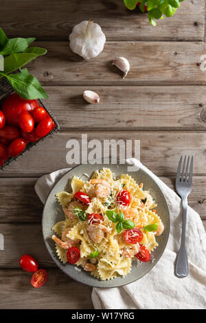 La pasta italiana le farfalle in una cremosa salsa di aglio con gamberetti, pomodori ciliegia e basilico su una piastra, vista dall'alto. Copia spazio per il testo. Rustico Foto Stock