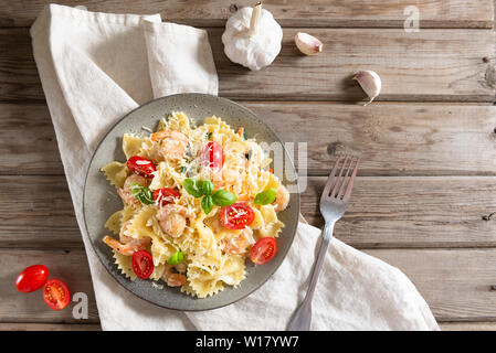 Farfalle con gamberetti, salsa di aglio, pomodorini e foglia di basilico sul tavolo in legno, cucina italiana, vista dall'alto. Copia spazio per il testo Foto Stock