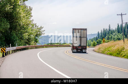 Big Rig bianco cabina giorno semi carrello con spoiler del tetto trasportano enormi coperte rinfusa semi rimorchio con scaletta sulla parete di fondo mobile sul vento di tornitura Foto Stock