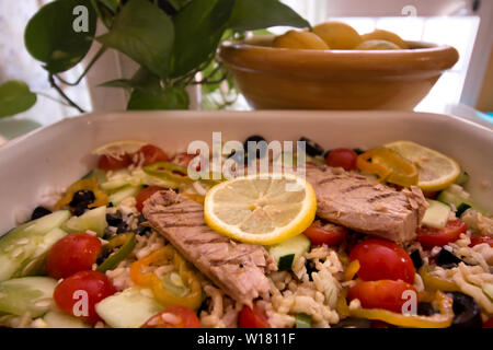 Gustosa insalata di riso con verdure fresche e grigliate di sgombro e sullo sfondo di un recipiente con limoni accanto a foglie verdi Foto Stock