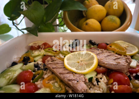 Gustosa insalata di riso con verdure fresche e grigliate di sgombro e sullo sfondo di un recipiente con limoni accanto a foglie verdi Foto Stock