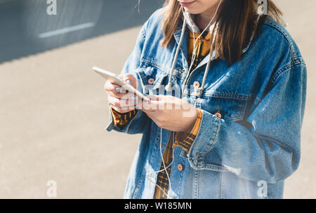 Felice giovane donna utilizzando i social media sui loro smartphone a piedi giù per una strada di città Foto Stock