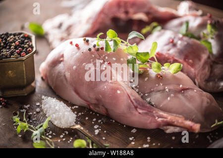 Materie cosce di coniglio sale pepe e le erbe su butcher board Foto Stock