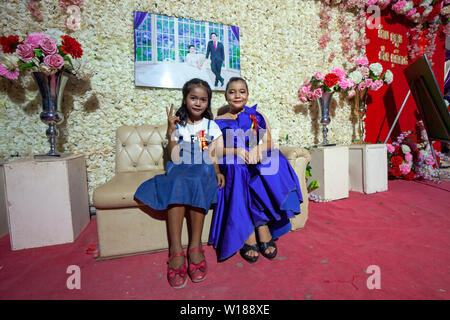 Due giovani ragazze cambogiane posano per una foto sotto una fotografia raffigurante la sposa e lo sposo a Khmer cerimonia di nozze in Siem Reap, Cambogia. Foto Stock