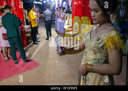 Una giovane donna cambogiano che indossano il tradizionale abito Khmer scatta una fotografia con una smart phone a una cerimonia di nozze a Siem Reap, Cambogia. Foto Stock