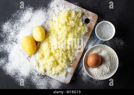 Scorza di patate bollite con farina, uova e sale per la preparazione di un piatto italiano - gnocchi di patate. Sfondo nero. Foto Stock