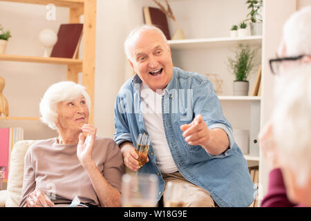 Felice l'uomo senior con flûte di champagne puntando al suo amico durante la conversazione a casa party Foto Stock