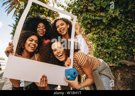 Un gruppo di giovani amici di sesso femminile in posa con vuoto cornice immagine. Ragazze sorridenti con vuoto photo frame all'aperto nella città. Foto Stock