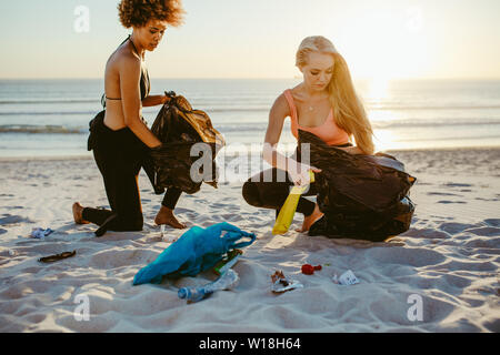 Due femmina surfers prelievo di lettiera sulla spiaggia. Volontari di sesso femminile la pulizia della spiaggia. Foto Stock