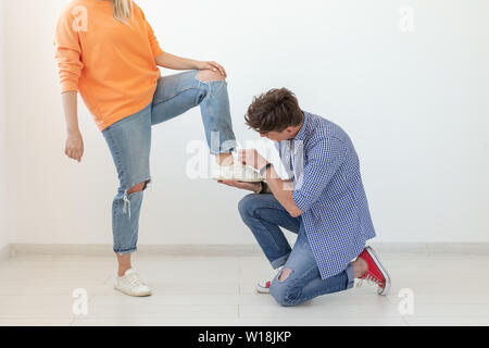 Giovane uomo è in ginocchio e riverenti legatura di lacci delle scarpe per il suo dominatore donna non identificato in posa su uno sfondo bianco. Nozione di posizione dominante Foto Stock