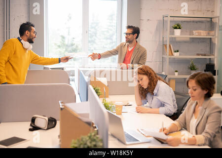 I dipendenti del dipartimento analitico lavoro in open space office: medio-orientali uomo passando la carta a un collega mentre le donne esaminando i documenti Foto Stock