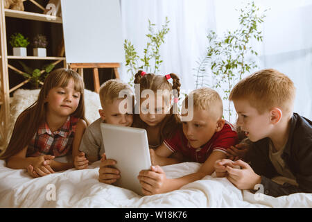 Ragazzi e ragazze utilizzando diversi gadget a casa. Childs con smart orologi, smartphone e cuffie. Rendendo selfie, chating, giochi, guardi i video. Interazione tra bambini e tecnologie moderne. Foto Stock