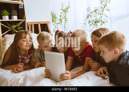 Ragazzi e ragazze utilizzando diversi gadget a casa. Childs con smart orologi, smartphone e cuffie. Rendendo selfie, chating, giochi, guardi i video. Interazione tra bambini e tecnologie moderne. Foto Stock