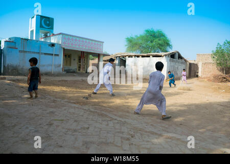 Rahimyar khan,punjab,pakistan-luglio 1,2019:alcuni ragazzi locali a giocare a cricket in un villaggio,battitore giocando un colpo,polvere battenti. Foto Stock