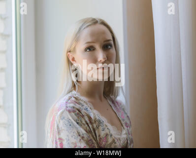 Malinconici donna in accappatoio seduta sul davanzale. Luce naturale. Foto Stock