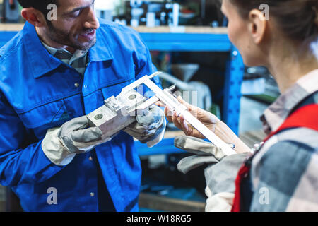 Donna e uomo lavoratore misurazioni di controllo di metallo del pezzo da lavorare Foto Stock