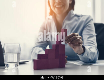 Sorridente imprenditrice costruire con successo un grafico finanziario utilizzando pezzi di legno, essa è aggiunta l'ultimo blocco Foto Stock