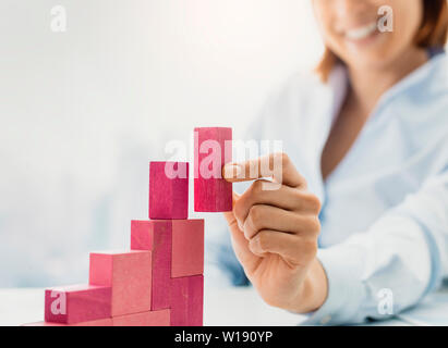 Sorridente imprenditrice costruire con successo un grafico finanziario utilizzando pezzi di legno, essa è aggiunta l'ultimo blocco Foto Stock