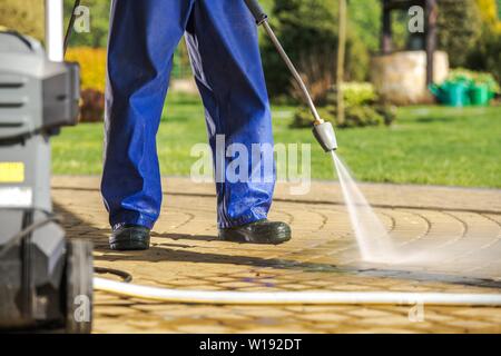 Il Lavoratore e la rondella a pressione. Gli uomini indossano cappotto di pioggia pulizia sentieri di mattoni utilizzando potenti spruzzatore di acqua. Foto Stock