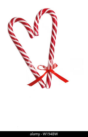 Candy canes formando un cuore con un po' di nastro su uno e isolato su sfondo bianco Foto Stock