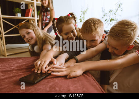 Ragazzi e ragazze utilizzando diversi gadget a casa. Childs con smart orologi, smartphone e cuffie. Rendendo selfie, chating, giochi, guardi i video. Interazione tra bambini e tecnologie moderne. Foto Stock