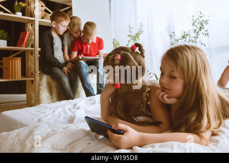 Ragazzi e ragazze utilizzando diversi gadget a casa. Childs con smart orologi, smartphone e cuffie. Rendendo selfie, chating, giochi, guardi i video. Interazione tra bambini e tecnologie moderne. Foto Stock