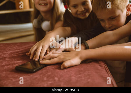 Ragazzi e ragazze utilizzando diversi gadget a casa. Childs con smart orologi, smartphone e cuffie. Rendendo selfie, chating, giochi, guardi i video. Interazione tra bambini e tecnologie moderne. Foto Stock