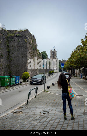 IOANNINA, Grecia - 6 giugno 2019 - il giovane femmina alti fotografo prende foto vicino alla strada stretta che circondano il vecchio castello della piccola e splendida città vecchia. Moto auto sfocata si avvicina Foto Stock