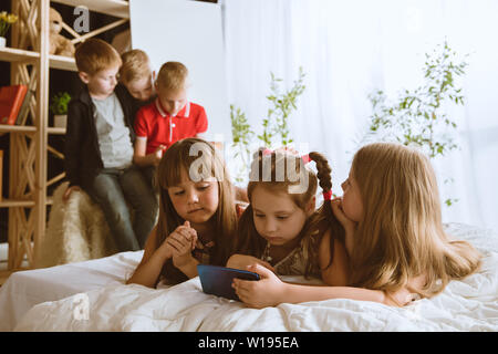 Ragazzi e ragazze utilizzando diversi gadget a casa. Childs con smart orologi, smartphone e cuffie. Rendendo selfie, chating, giochi, guardi i video. Interazione tra bambini e tecnologie moderne. Foto Stock