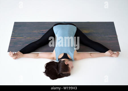 La donna caucasica fare yoga divide upavistha konasana sul tappetino fitness. Foto Stock