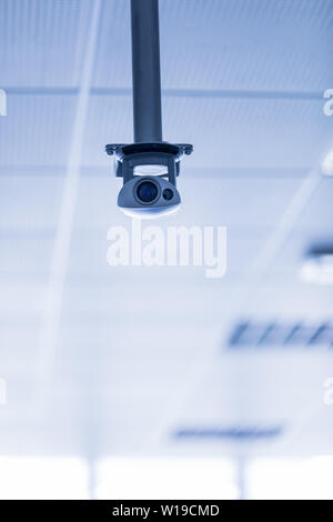 Singola telecamera di sorveglianza TVCC o sospesi dal soffitto su una staffa metallica contro un nei toni del blu con uno sfondo con spazio di copia Foto Stock