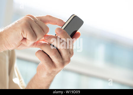 Le mani di un uomo maturo con un telefono cellulare la navigazione touchscreen contro un elevato la chiave sfondo sfocato Foto Stock