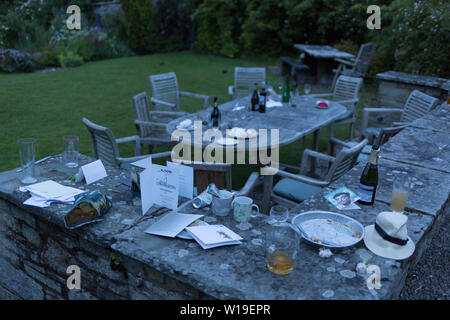 I postumi residui di bicchieri, bottiglie e le piastre all'alba, la mattina dopo un cinquantesimo compleanno, sparsi intorno al giardino nell'Herefordshire campagna, il 23 giugno 2019, a Kington, Herefordshire, Inghilterra. Foto Stock