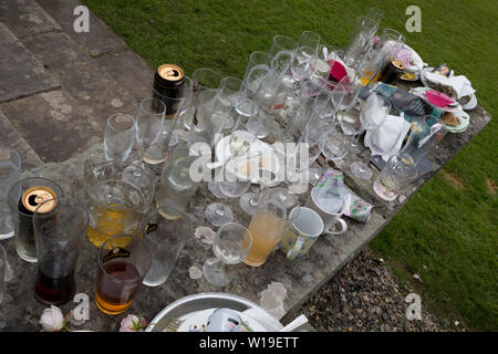 I postumi residui di bicchieri, bottiglie, lattine e le piastre, la mattina dopo un cinquantesimo compleanno, sparsi intorno al giardino nell'Herefordshire campagna, il 23 giugno 2019, a Kington, Herefordshire, Inghilterra. Foto Stock