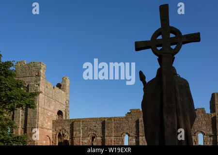 La statua di San Aidan di Lindisfarne dall'artista kathleen Parbury (1958) e le pareti in rovina di Lindisfarne Priory, sull Isola Santa il 27 giugno 2019, sull isola di Lindisfarne, Northumberland, Inghilterra. Il Santo Isola di Lindisfarne, nota anche semplicemente come Isola Santa è un'isola di fronte alla costa nord-est dell'Inghilterra. A Isola Santa ha una storia registrata a partire dal VI secolo D.C. fu un importante centro di cultura celtica e Anglo-sassone il cristianesimo. Dopo le invasioni dei Vichinghi e la conquista normanna dell'Inghilterra, un priorato è stato ristabilito. Foto Stock