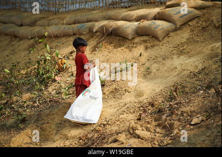 Bambino in abito rosso la raccolta di legna da ardere in Rohingya Refugee Camp Kutupalong, Bangladesh Foto Stock