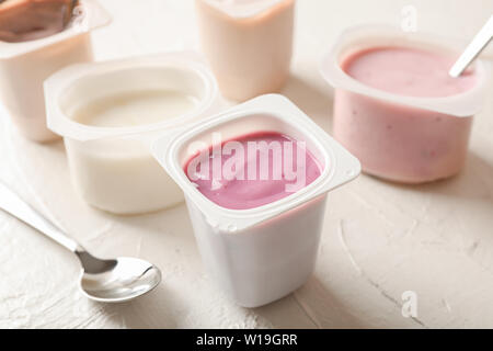 Composizione con i bicchieri di plastica con yogurt sul tavolo bianco Foto Stock