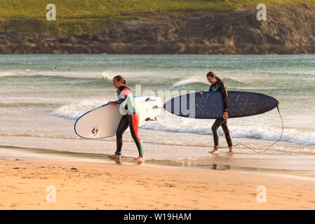 Surfisti femmina a piedi al di fuori del mare portando le loro tavole da surf a Fistral Beach in Newquay in Cornovaglia. Foto Stock