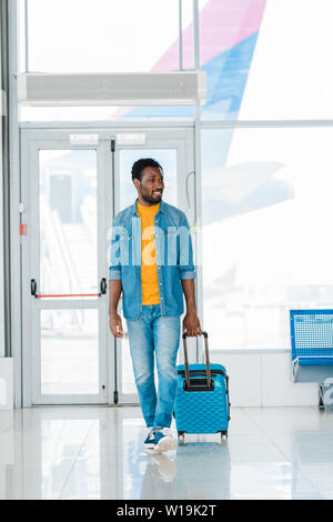 Sorridendo felice african american uomo a camminare con la valigia lungo la sala di attesa in aeroporto Foto Stock