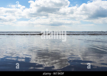 Una bella riflessione di blue skies nel Galles del Sud, Swansea come le maree lentamente si insinua fino alla spiaggia nel primo pomeriggio. Foto Stock