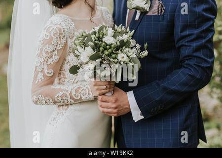 Immagine ritagliata della sposa e lo sposo abbracciando il giorno delle nozze. Appena una coppia sposata in amore azienda elegante bouquet di nozze. Foto Stock