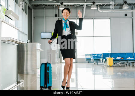 Africa sorridenti hostess americana con borsa da viaggio agitando la mano in aeroporto Foto Stock