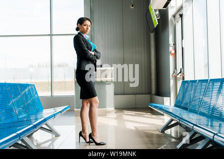 Bella African American hostess in piedi con le braccia conserte in aeroporto Foto Stock