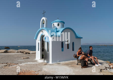 Kalamki Beach, Creta, Grecia. Giugno 2019. Giovane seduto al di fuori del blu e del bianco fishermans cappella a Kalamaki Harbour, a nord di Creta. Foto Stock